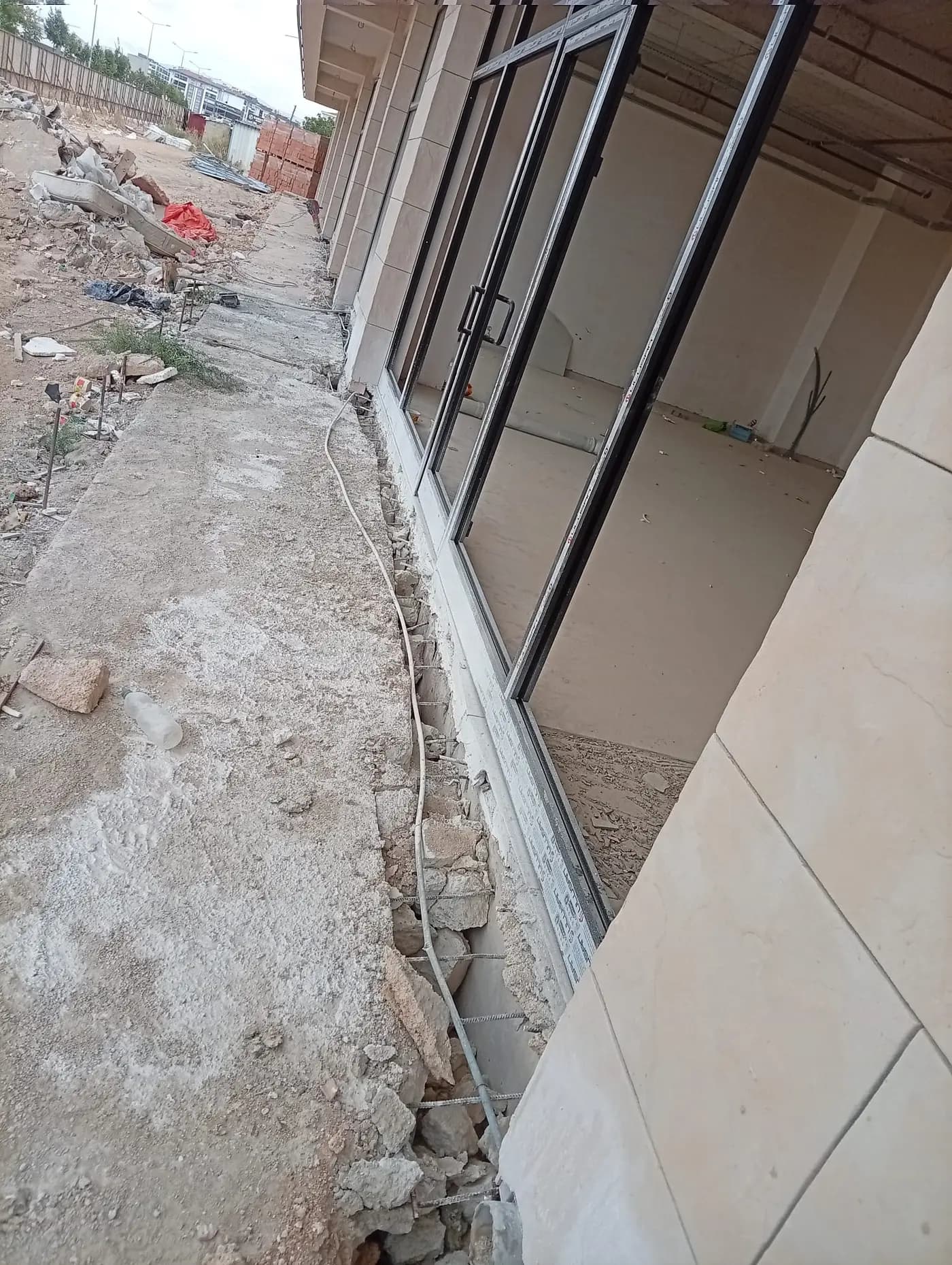 Doğrama hattı boyunca sökülmüş beton ve açığa çıkan düşey donatılar, arkada kaba yapısı biten iç mekân