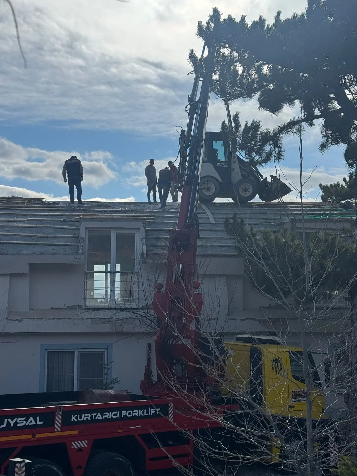 Teleskopik vinçle bina çatısına kaldırılmış mini yükleyici ve çatı üzerinde bekleyen ekip