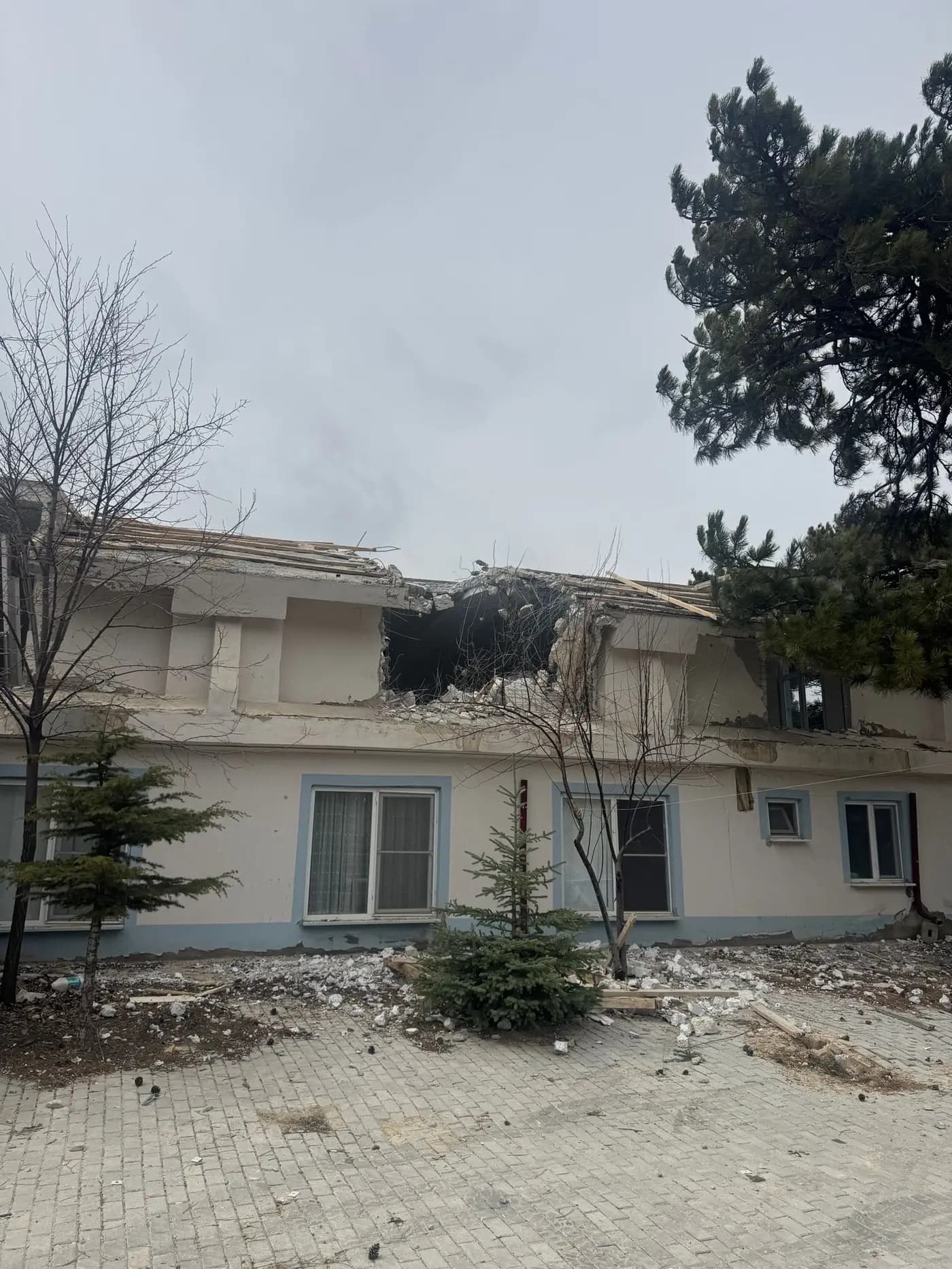 Çatı örtüsü sökülmüş bina gövdesi ve söküm için konumlanmış iş makineleri