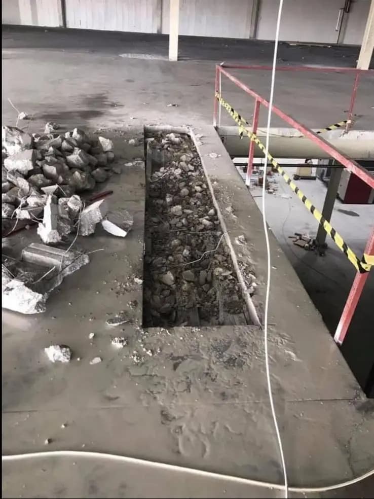 Zemin betonu kaldırılarak açılmış uzun dikdörtgen boşluk, kenarda toplanmış moloz yığını ve kırmızı korkuluk