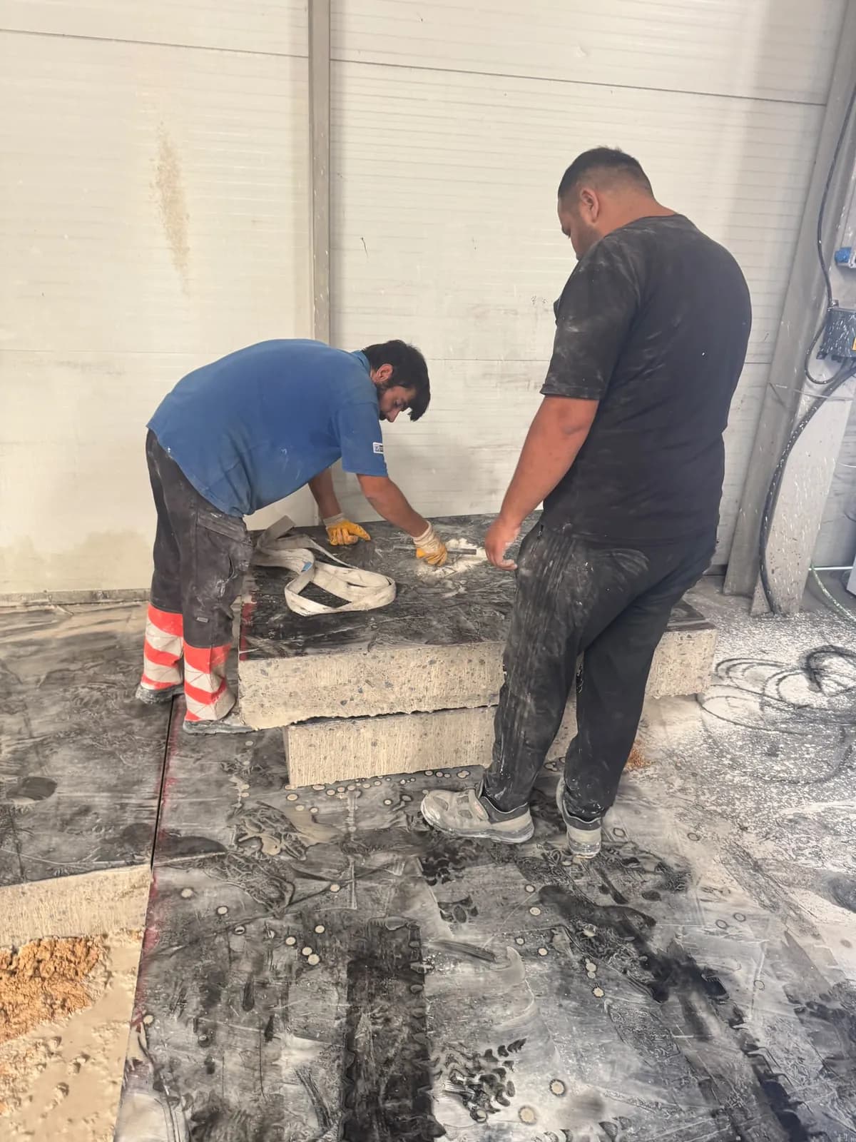 İki personelin kesilmiş beton plakaya kaldırma sapanı bağlaması; plaka kalınlığı kesit yüzeyinde görülüyor