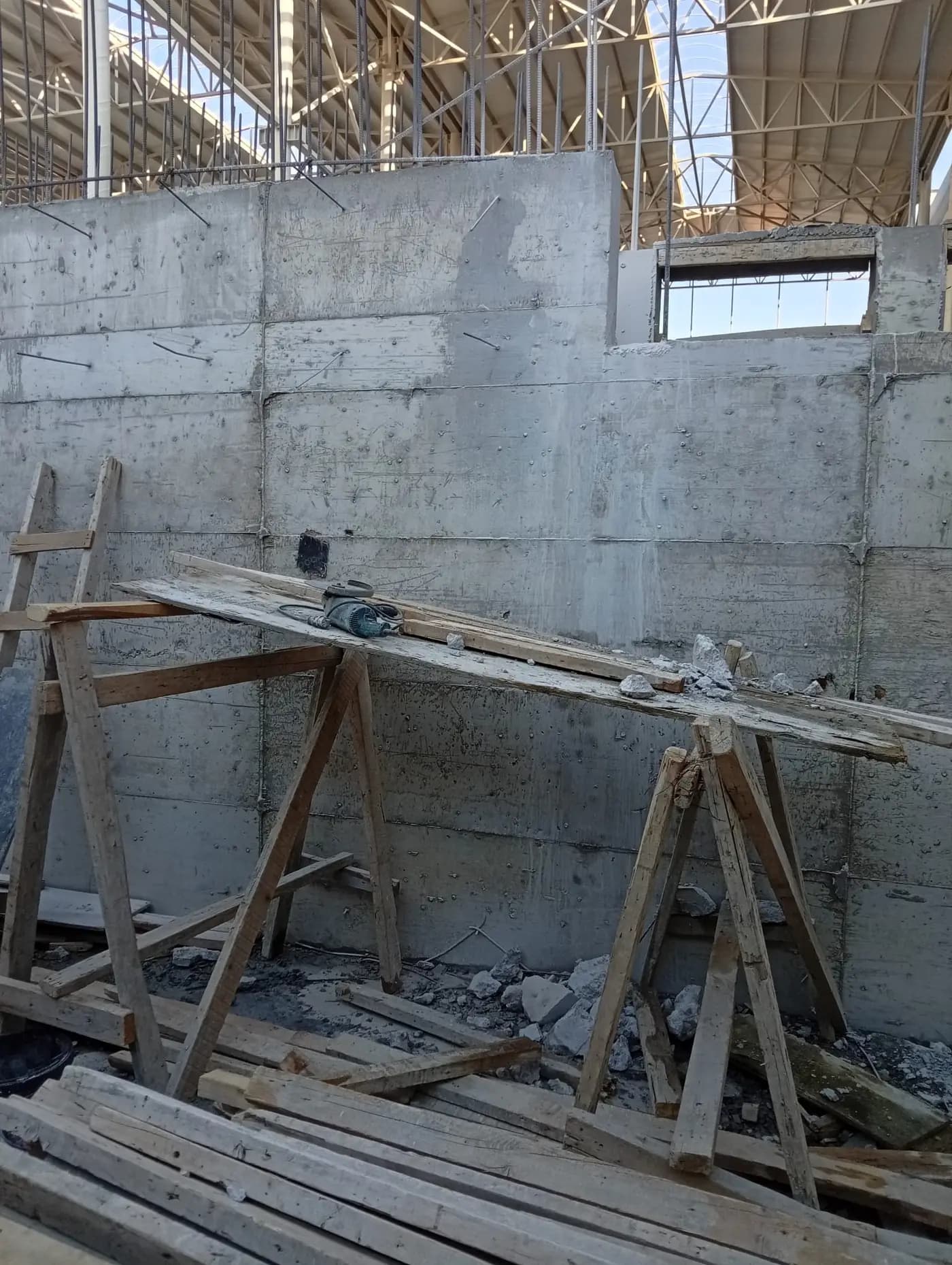 Kapalı hacimde kalıp izleri görünen betonarme perde duvar ve önünde kurulu ahşap sehpa üzerindeki kesme ekipmanı
