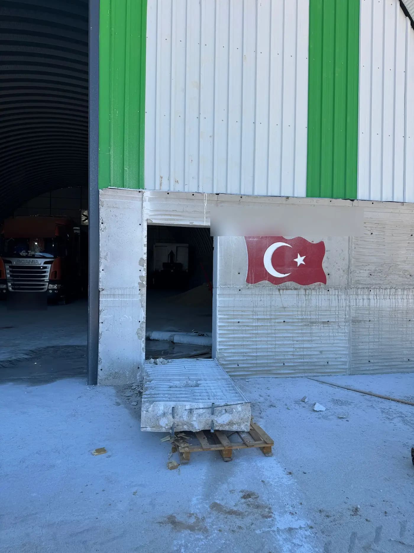 Depo dış cephesinde tamamlanmış kapı boşluğu ve önünde paletler üzerinde duran kesilmiş panel parçası