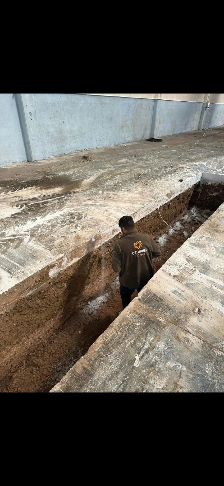 Kapalı hacimde açılmış hat hendeğinin içinde duran Özturhan Karot montlu ekip üyesi ve düz kesilmiş beton kenarları
