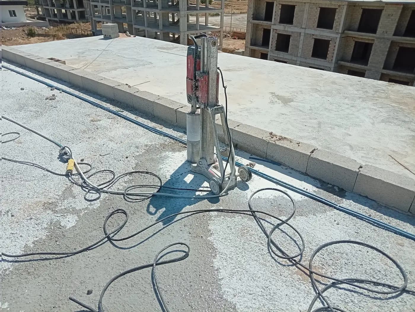 Yapım aşamasındaki binanın çatı döşemesinde parapet dibine kurulmuş sehpalı karot makinesi ve döşemede serili kablolar