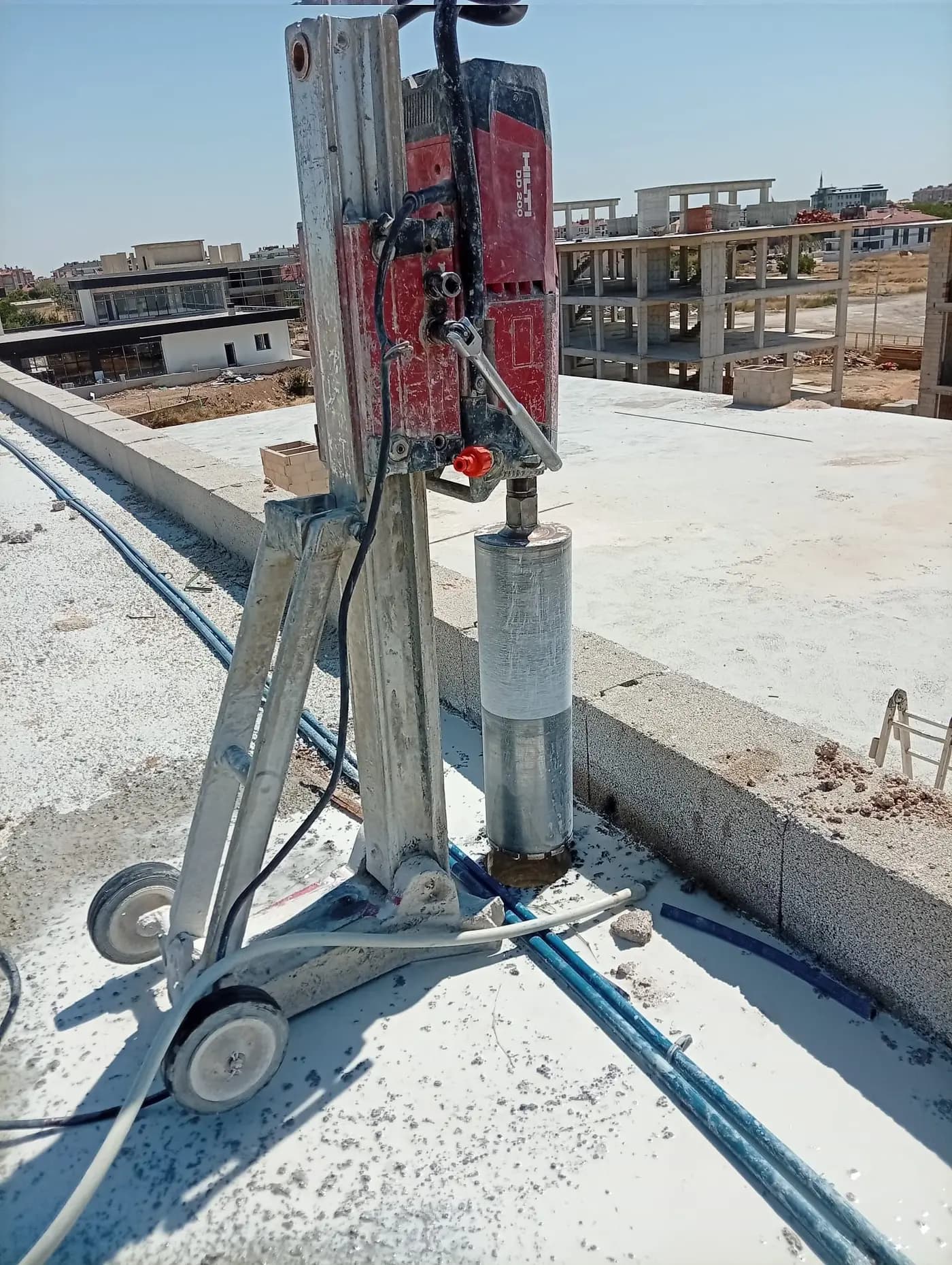 Döşemeye inmiş elmas karot ucuyla çalışan Hilti DD 200 makinesinin yakın görünümü ve arkada yapım aşamasındaki binalar