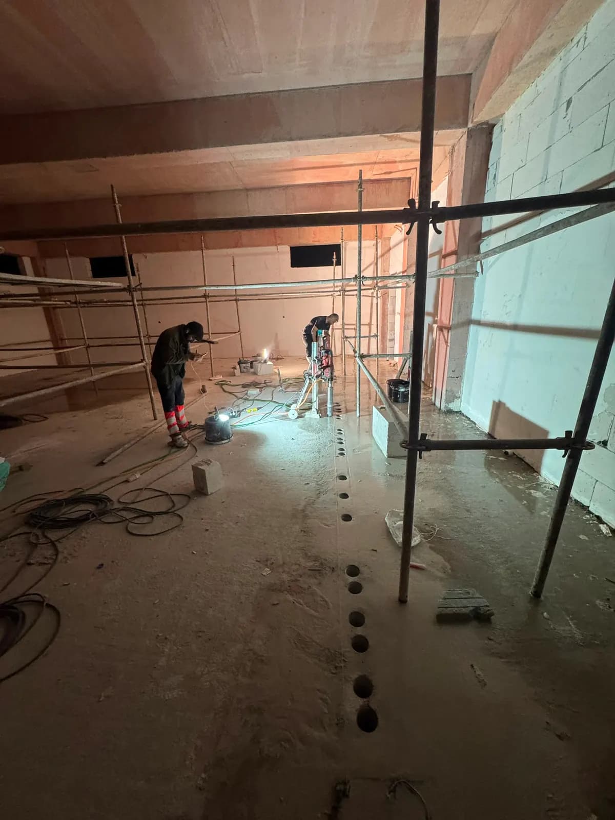 İskele kurulu kapalı hacimde karot makinesiyle döşemede sıralı delik açan iki kişilik ekip