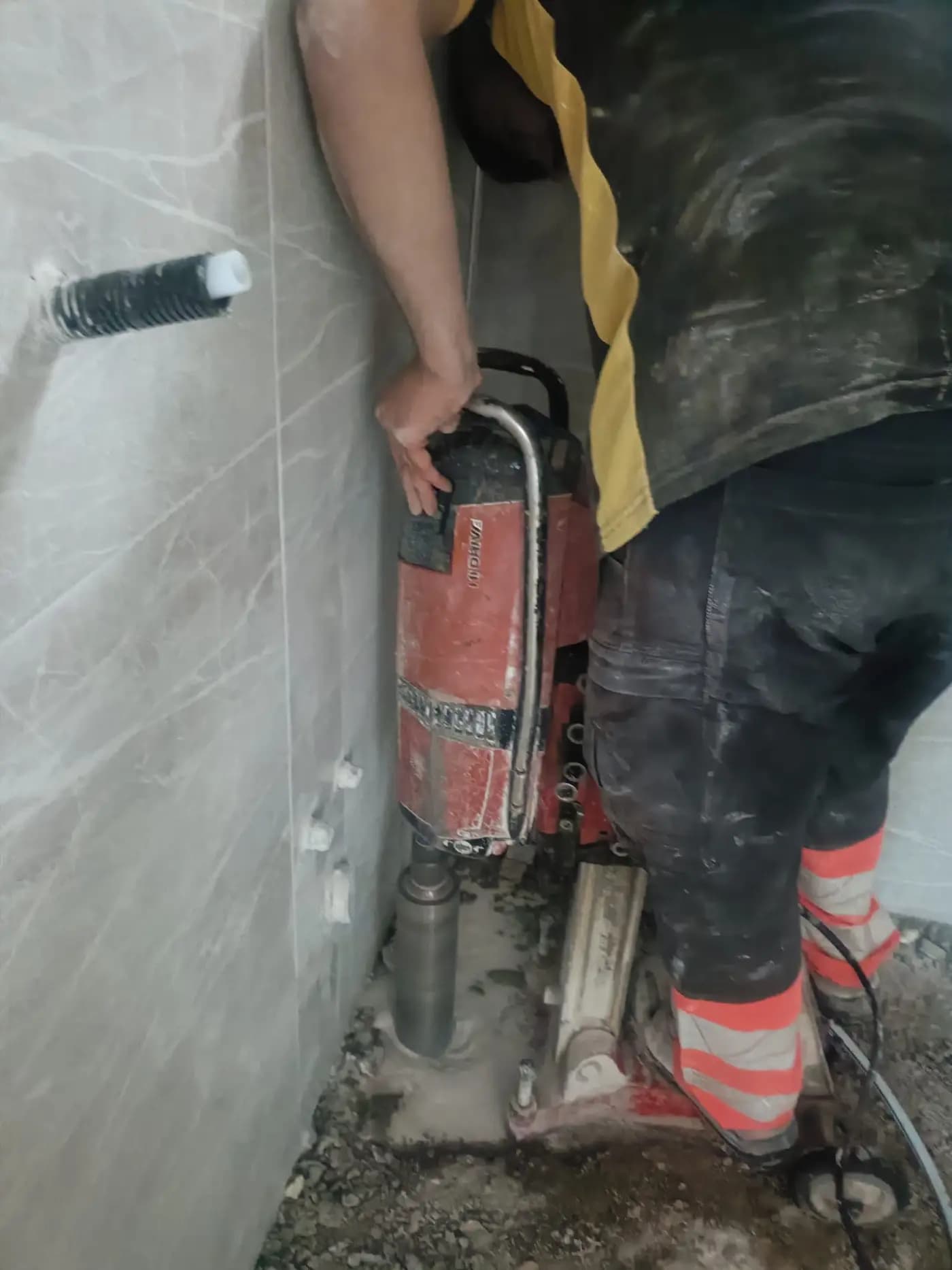 Fayans kaplı duvarda karot makinesiyle delme yapan personel ve duvardan çıkan yalıtımlı tesisat borusu