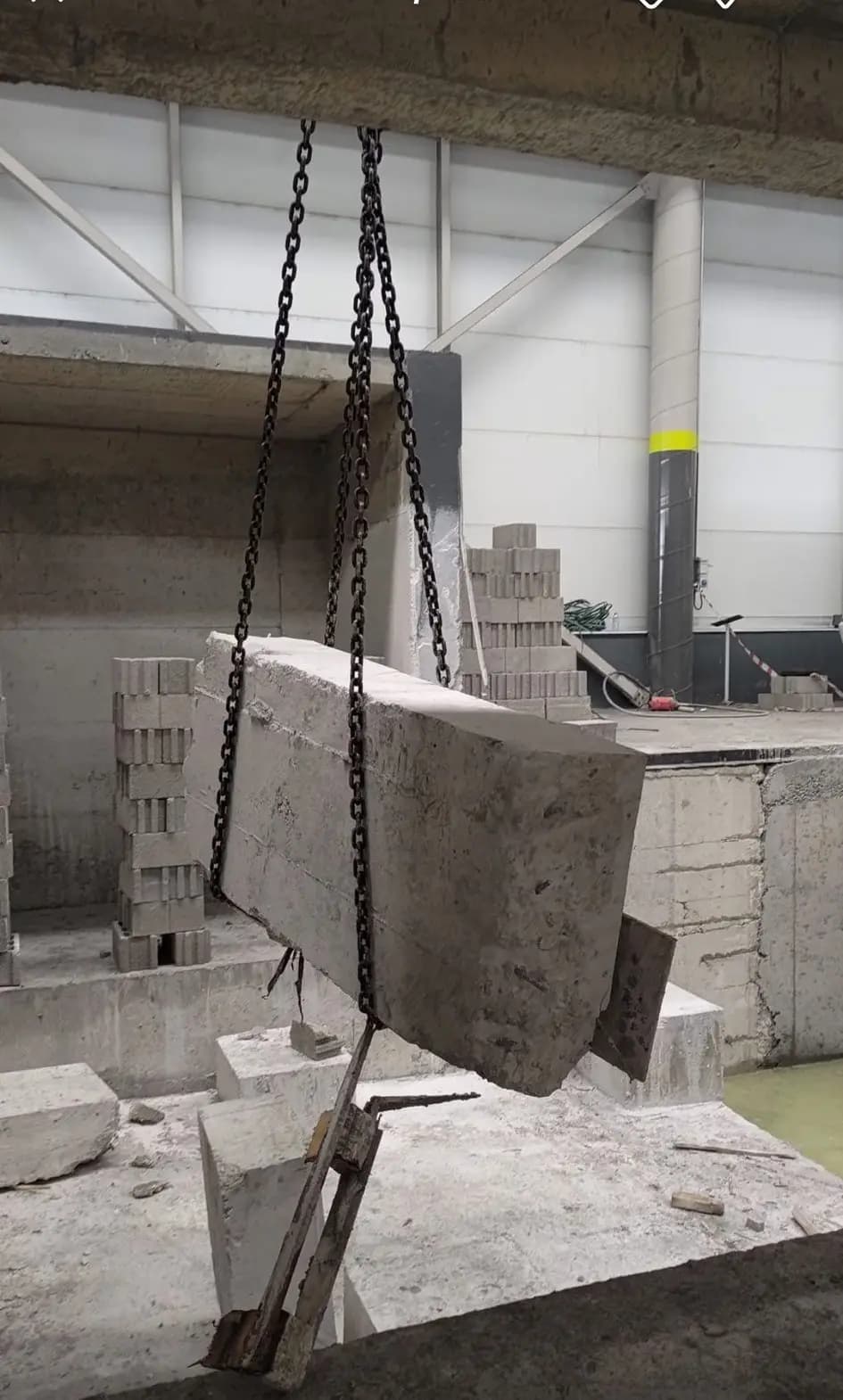 Zincir sapanla askıya alınmış büyük betonarme blok ve arkada briket istifleriyle desteklenmiş kesim alanı