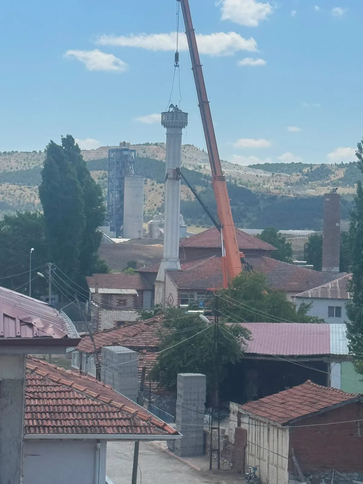 Yerleşim dokusu içinde vinçle askıya alınmış minare gövdesinin uzaktan görünümü