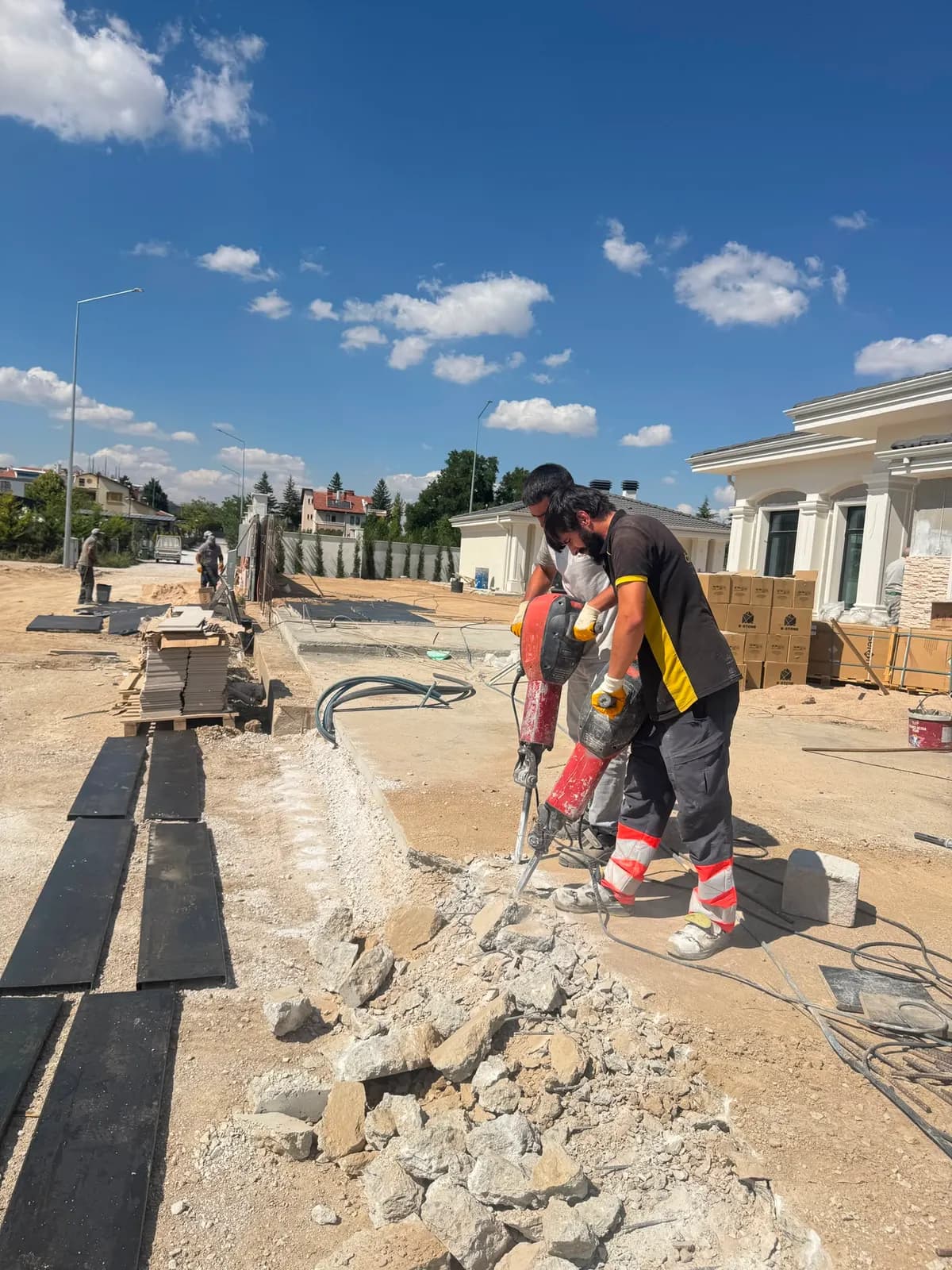 Yapım hâlindeki yapının önünde kırıcılarla saha betonunu söken iki personel