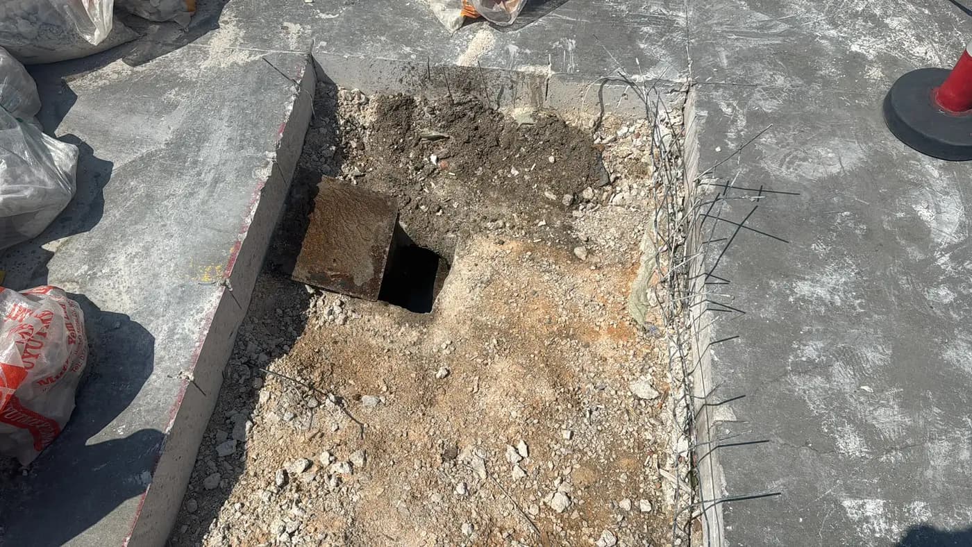 Saha betonunda açılmış kare rögar boşluğu, kenarında yukarı bükülmüş donatılar ve trafik konisi