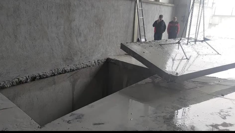 Plakanın alınmasıyla açığa çıkan dikdörtgen döşeme boşluğu ve kenarda bekleyen iki kişi